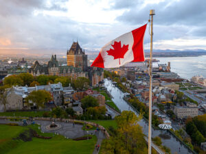 A flowing Canadian flag on a flagpole. Taken at sunset with Old Quebec City and the St. Lawrence River in the background. Aerial HDR view.